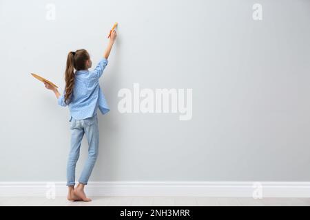 Une petite fille peint sur un mur lumineux à l'intérieur, vue arrière. Espace pour le texte Banque D'Images