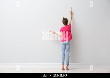 Une petite fille peint sur un mur lumineux à l'intérieur, vue arrière. Espace pour le texte Banque D'Images