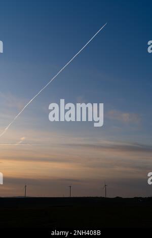 Coucher de soleil dans la campagne avec des éoliennes et un avion avec des contrailles dans le ciel bleu Banque D'Images