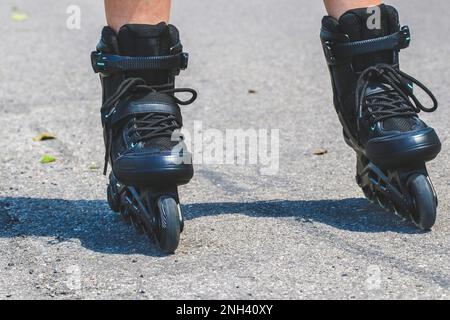 Jambes de femme qui apprend le patinage en ligne sur la route de l'asphalte Banque D'Images