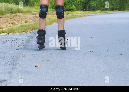 Jambes de femme qui apprend le patinage en ligne sur la route de l'asphalte Banque D'Images