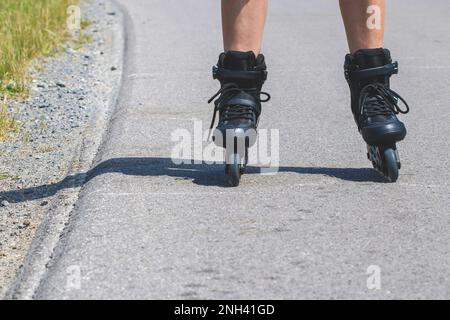 Jambes de femme qui apprend le patinage en ligne sur la route de l'asphalte Banque D'Images