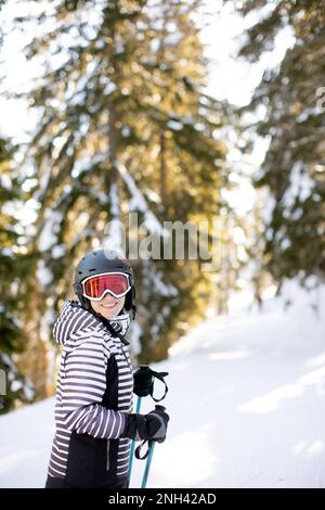 Jeune femme qui profite de la journée d'hiver pour skier sur les pistes enneigées, entourée de grands arbres et habillée pour les températures froides Banque D'Images