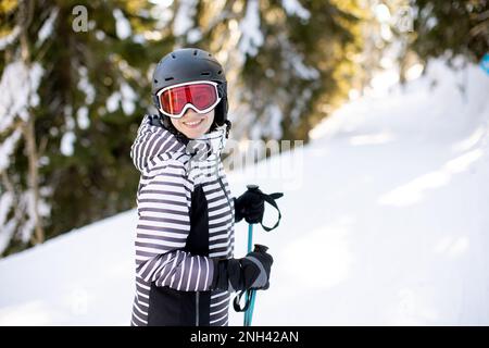 Jeune femme qui profite de la journée d'hiver pour skier sur les pistes enneigées, entourée de grands arbres et habillée pour les températures froides Banque D'Images