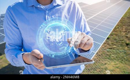 Ingénieur méconnaissable avec une tablette avec hologramme HUD de terre dans une usine de panneaux solaires photovoltaïques. Banque D'Images