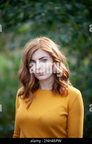 Une femme à tête rouge portant un pull de couleur moutarde à l'extérieur Banque D'Images