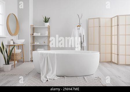 Baignoire moderne, lavabo, peignoir et étagères avec accessoires dans la salle de bains Banque D'Images