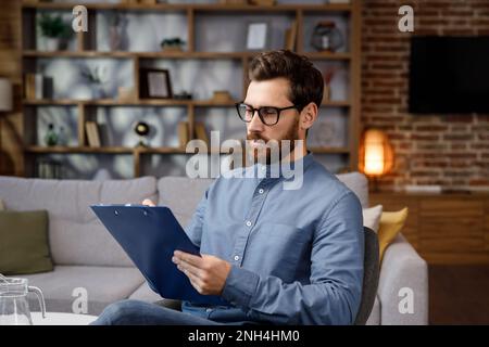 Un homme beau adulte s'assoit à la maison dans un bureau élégant. Psychologue, coach ou homme d'affaires regardant la caméra et souriant. Belles dents et Banque D'Images