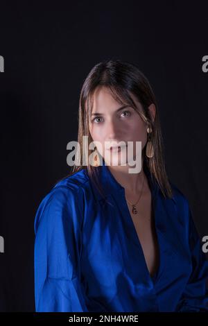 belle jeune femme vêtue de fond bleu et noir regarde droit devant avec un regard et de jolis yeux Banque D'Images