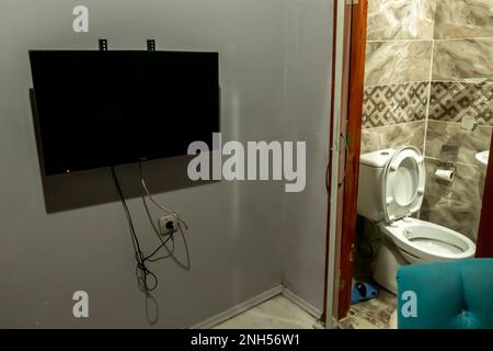 Simple et bizarre chambre d'hôtel avec TV sur un mur à côté de la salle de bains des toilettes Banque D'Images