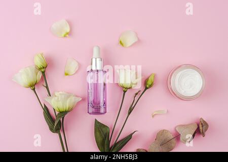 Bouteille cosmétique violette, pot crème, fleurs d'eustome blanc et feuilles d'eucalyptus sur fond rose. Vue de dessus, plan d'agencement. Banque D'Images