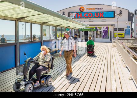 BOURNEMOUTH, Royaume-Uni - 08 juillet 2022. Un couple âgé se promègne à Bournemouth Pier, avec une femme sur un scooter pour personnes à mobilité réduite. Vieillesse et invalidité Banque D'Images