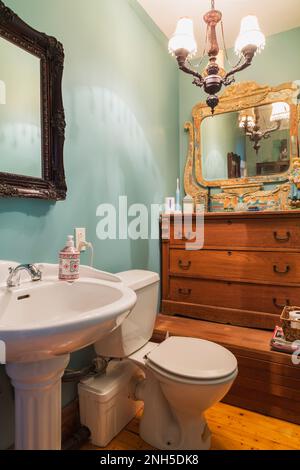 Lavabo sur pied blanc avec toilettes électriques, miroir en bois ancien et commode dans la salle de bains avec parquet en bois de pin dans la salle de bains à l'étage. Banque D'Images