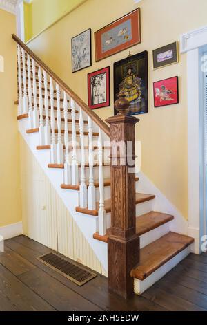 Escalier en bois de pin avec balustres peints en blanc et garde-corps en chêne coloré et poste de newel dans la salle de séjour à l'intérieur de la maison de style québécois datant de 1830. Banque D'Images