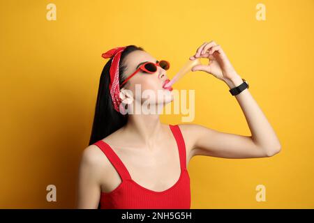 Jeune femme à la mode dans une tenue à épingler mâchant du bubblegum sur fond jaune Banque D'Images