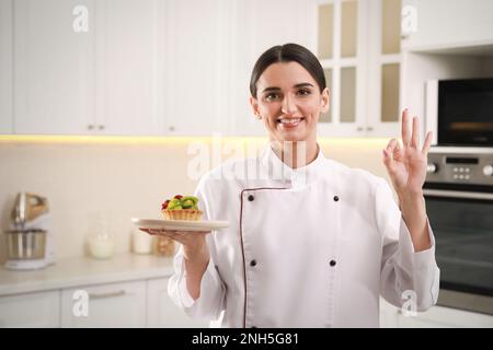 Confiserie professionnelle heureuse avec tartelette montrant un geste correct dans la cuisine Banque D'Images