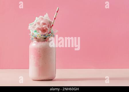 Délicieux milkshake aux fraises dans un pot en verre, recouvert d'un coton bonbon sur fond rose Banque D'Images