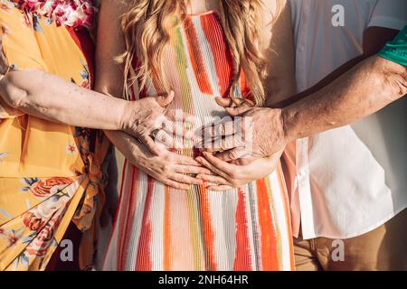 Gros plan de la femme enceinte avec les mains de sa famille touchant son ventre. Porter une robe Banque D'Images