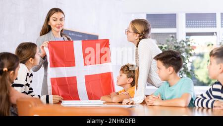 Le professeur d'école parle aux élèves du Danemark et détient un drapeau du Danemark entre les mains. Banque D'Images
