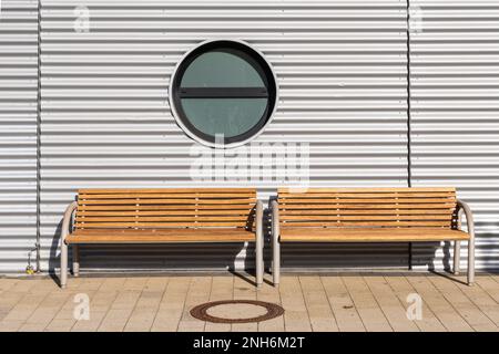 Deux bancs en bois le long d'un mur ondulé. Fenêtre ronde dans le mur. Banque D'Images