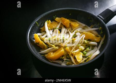 Chicorée frite avec des morceaux d'orange et des oignons de printemps dans une poêle noire sur la cuisinière, repas végétarien sain pour un régime naturel bas de carb, copie de spac Banque D'Images