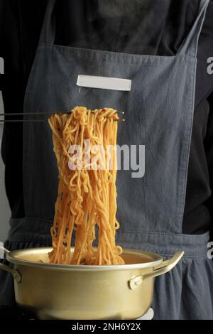 Femelle utilisant des pinces en acier inoxydable pour cuire le ramyeon ou le soupe de nouilles instantanées coréennes dans un pot en aluminium jaune coréen à double poignée sur cuisinière à gaz Banque D'Images