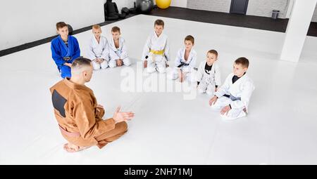 Groupe de petits garçons, enfants dans un kimono assis au sol autour de l'autocar. Les enfants s'entraîne à l'intérieur. Judo, entraînement de jiu-jitsu Banque D'Images