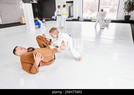 Portrait dynamique de l'homme, judo professionnel, entraînement de l'entraîneur de jiu-jitsu avec petit garçon, enfant dans un kimono blanc. Style de vie sportif Banque D'Images