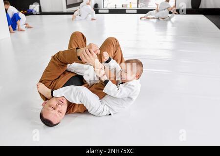 Portrait dynamique de l'homme, judo professionnel, entraînement de l'entraîneur de jiu-jitsu avec petit garçon, enfant dans un kimono blanc. Enseigner l'endurance et la force aux enfants Banque D'Images