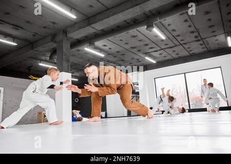 Portrait dynamique de l'homme, judo professionnel, entraînement de l'entraîneur de jiu-jitsu avec petit garçon, enfant dans un kimono blanc. Les enfants font des exercices Banque D'Images