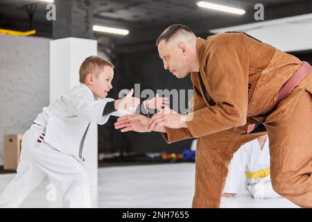 Portrait dynamique de l'homme, judo professionnel, entraînement de l'entraîneur de jiu-jitsu avec petit garçon, enfant dans un kimono blanc. Occupation sportive Banque D'Images