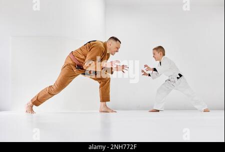 Portrait dynamique de l'homme, judo professionnel, entraînement de l'entraîneur de jiu-jitsu avec petit garçon, enfant dans un kimono blanc. Style de vie sportif Banque D'Images