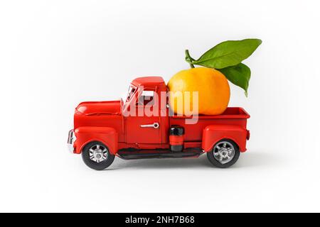 Orange mandarine orange avec une branche verte avec des feuilles dans un camion de Noël rouge sur fond blanc. Concept - carte de vœux pour Noël et New Y. Banque D'Images