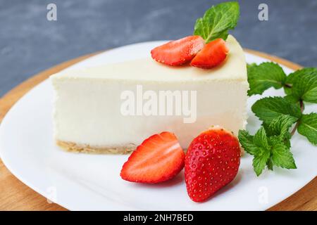 Cheesecake classique New York morceau de cheesecake en tranches avec des fraises fraîches et de la menthe sur une assiette blanche sur un fond bleu classique. Gros plan. Sélection Banque D'Images