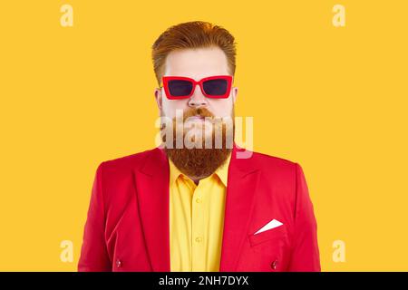 Portrait de l'homme chubby à barbe grave drôle en costume rouge, chemise jaune et lunettes de soleil funky Banque D'Images