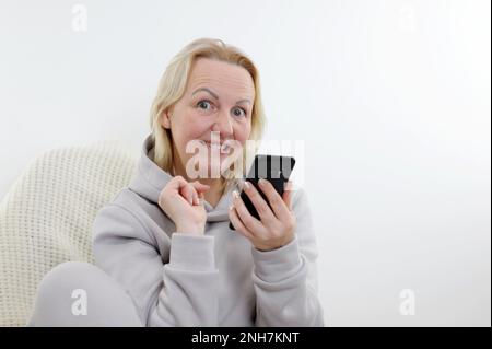 La femme a l'idée d'acheter un cadeau pour elle-même, elle regarde dans le cadre levant les yeux ouverts mordant la lèvre et slily tenant le téléphone dans les mains appel ordre rêve réalisation de désir Banque D'Images