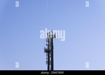 Tour de télécommunications avec antennes cellulaires et répéteurs contre un ciel bleu clair avec deux traces d'avions volants Banque D'Images
