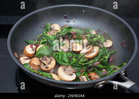 Champignons, oignons rouges et épinards frits dans une poêle sur un four à convection Banque D'Images