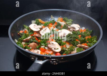 Kale, champignons, oignons et poivrons rouges frits dans une poêle sur un four à convection Banque D'Images