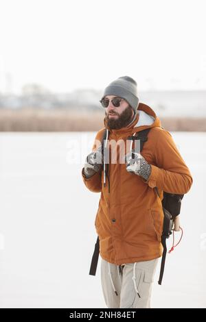 Un homme barbu avec un sac à dos en vêtements chauds d'hiver marche sur un lac gelé en hiver. Le concept de randonnée et de mode de vie actif. Banque D'Images