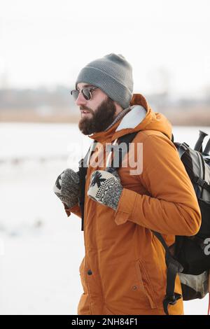 Un homme barbu avec un sac à dos en vêtements chauds d'hiver marche sur un lac gelé en hiver. Le concept de randonnée et de mode de vie actif. Banque D'Images