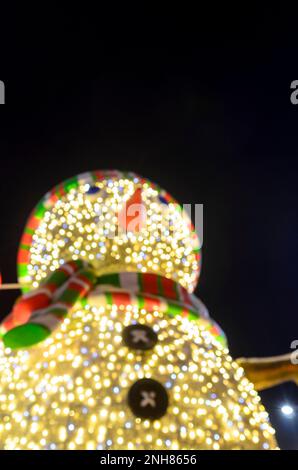 Des bonhomme de neige aux couleurs vives avec une casquette rayée et un foulard, avec des boutons noirs et un nez de carotte ont soulevé une main accueillante dans des gants. Banque D'Images