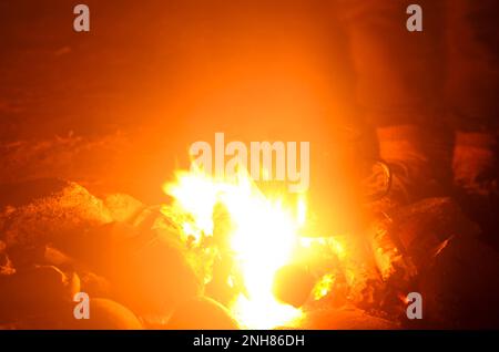 Silhouette floue des pieds d'une personne autour du feu de camp. Banque D'Images