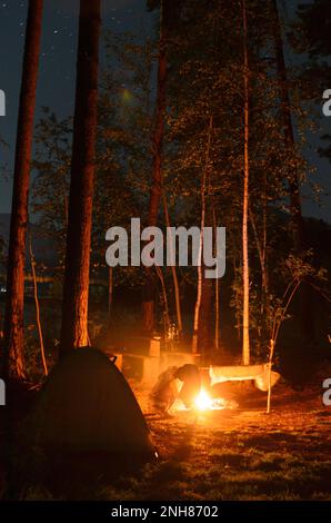 Le feu près de la tente et la silhouette d'une personne fille au repos sur la nature la nuit. Les choses sèchent par la flamme, et entre les branches Banque D'Images