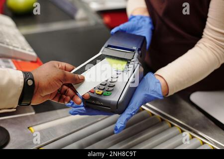 Gros plan de la caissière féminine en porte-cartes avec des gants, tandis que les jeunes Afro-américains paient pour les produits Banque D'Images