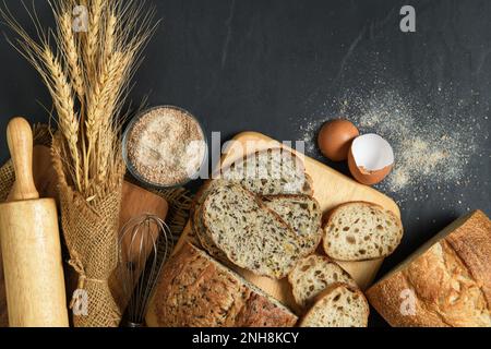 Faire glisser le pain de levain multi-grain et la baguette en tranches avec la farine de blé entier sur fond de pierre noire, concept de boulangerie maison Banque D'Images