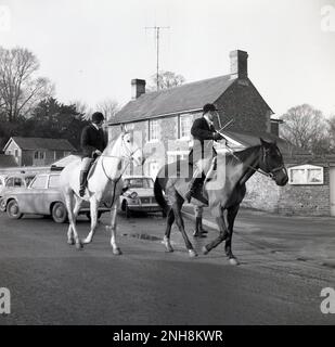 1965, historique, Thurlow Hunt, hommes et femmes chassent des maîtres sur leurs chevaux sur une ruelle de campagne, Thurlow, Angleterre, Royaume-Uni. Les orgues de la chasse du Thurlow remontent au siècle 18th, la chasse ayant lieu sur les terres arables et les prairies qui se trouvent à la fois dans le Suffolk et à Cambridge. Voitures de l'époque, y compris une Ford Anglia garée sur le côté de la route. Banque D'Images