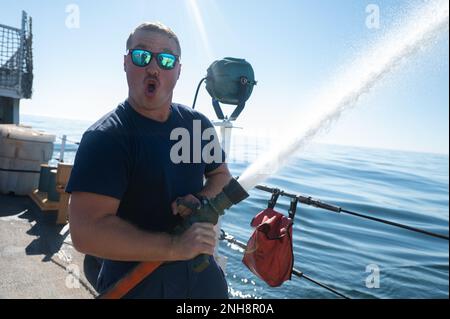 ÉTATS-UNIS Garde côtière Petty Officer 1st classe Cory Demery, un spécialiste de l'application de la loi maritime à bord de l'ours USCGC (WMEC 901), réagit à la pressurisation soudaine de l'eau dans son tuyau d'incendie, dans l'océan Atlantique, au 27 juillet 2022. Demery a aidé les copains de l'arme à feu à effectuer l'entretien du système sprinkleur du magazine du navire. Banque D'Images