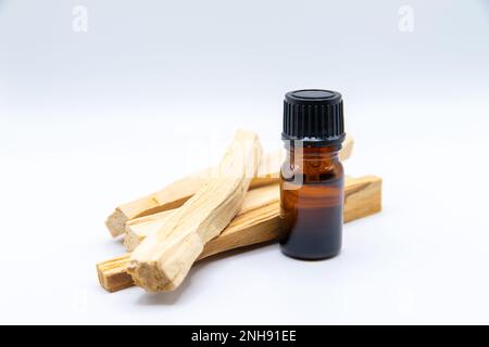 Palo Santo (Saint-Stick) extrait d'huile essentielle Essense dans une bouteille avec des bâtons de Palo Santo à côté. Gros plan isolé sur fond blanc. Banque D'Images
