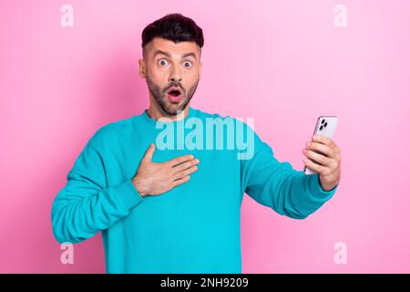 Portrait d'un homme confus choqué bras toucher poitrine bouche ouverte tenir téléphone isolé sur fond rose Banque D'Images